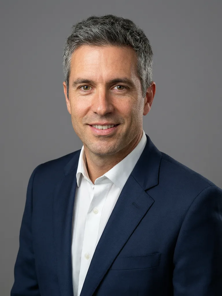 Qwen Image 3: Professional corporate headshot of a man in his forties with short salt-and-pepper hair, wearing a navy suit and a white shirt, with a slight smile, against a neutral mid-gray seamless backdrop. Soft key light from the left with a gentle fill, sharp focus on the eyes, shallow depth of field.